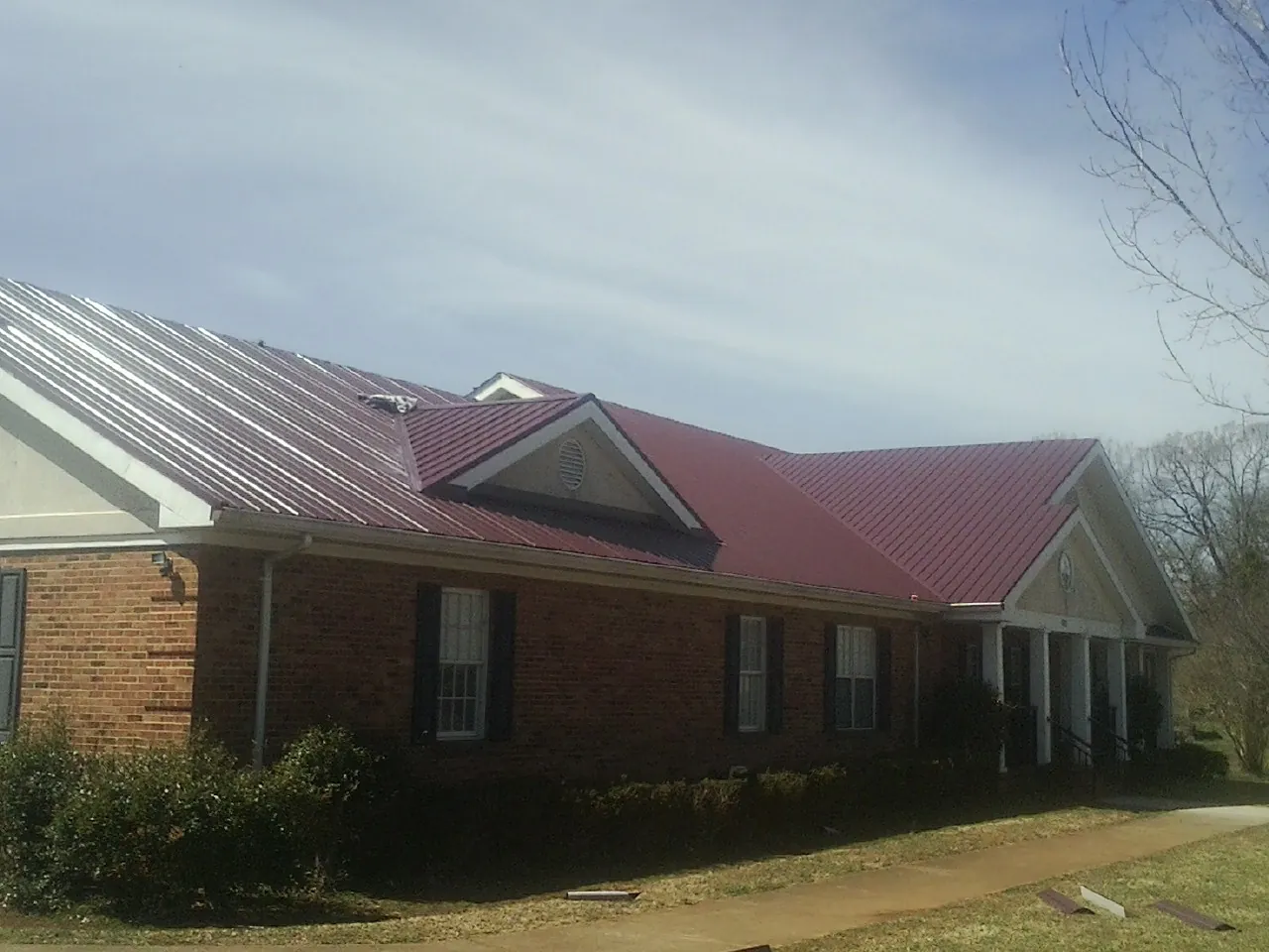 Red metal roof with gabled entries on a long brick building, from a Hail Damage Roof Repair job in Crawfordsville