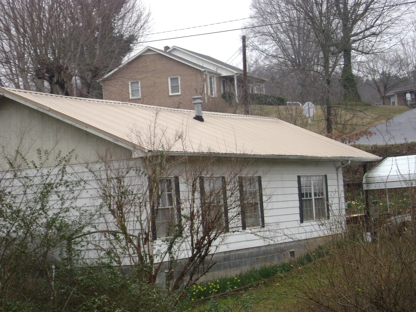 Tan metal roof on a white sided house set into a hillside — Commercial Roofing by Roofing Brothers in Crawfordsville